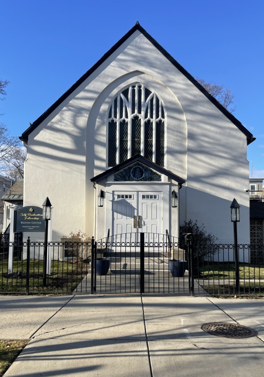 Front facing entrance of a white church building with triangular roof and black wrought iron fence in front. Sign that says Self-Realization Fellowship Boston Center Founded by Paramahansa Yogananda