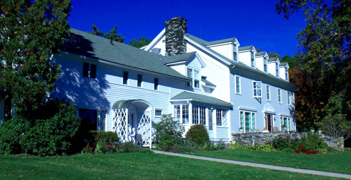 front of large white house with green lawn in front and trees both sides
