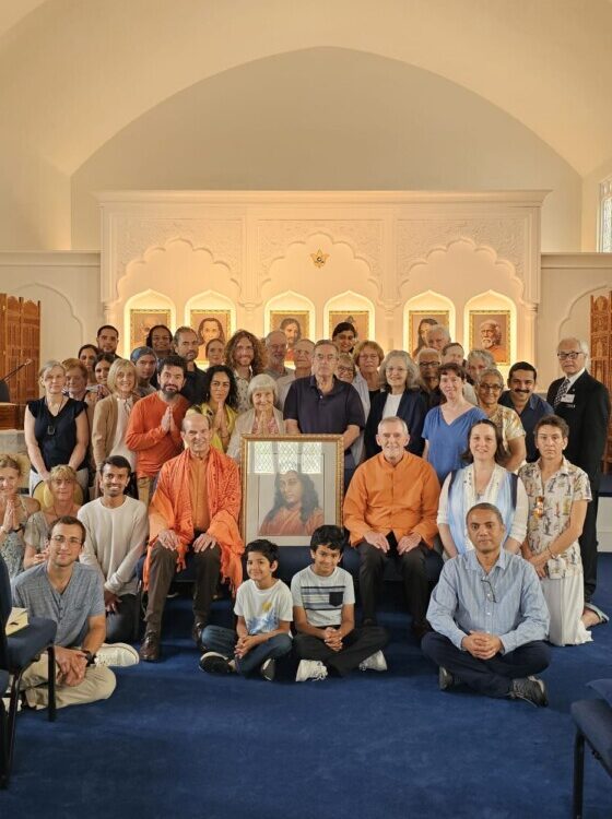 Photo of altar with photo of Paramahansa Yogananda in front. Frame is draped with flower garland and surrounded by flowers. Altar behind with photos of Lahiri Mahasaya, Babaji, Jesus Christ, Bhagavan Krishna, Paramahansa Yogananda and Swami Sri Yukteswar.