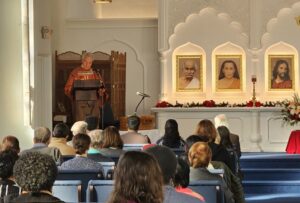 image people sitting in chairs in rows with an altar in front of them and a robed speaker at a podium